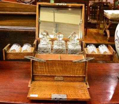 Lot 612 - An early 20th century blond oak tantalus cabinet, set with three hobnail cut decanters and with...
