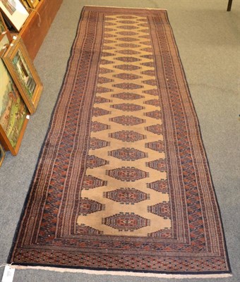 Lot 1233 - A narrow Lahore Buhkara runner, Punjab, The camel field with a column of salor guls enclosed by...