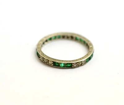 Lot 177 - An emerald and diamond eternity ring, trios of step cut emeralds and alternate with trios of...