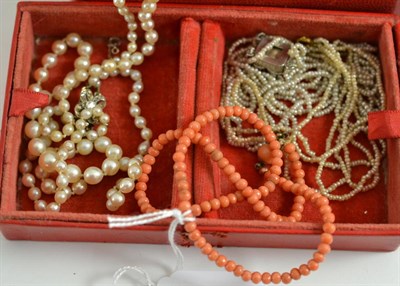 Lot 222 - A red jewellery box containing two seed pearl necklaces, a cultured pearl necklace and a coral...