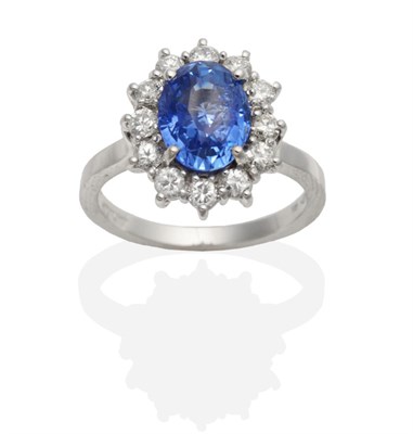 Lot 469 - An 18 Carat White Gold Sapphire and Diamond Cluster Ring, an oval cut sapphire within a border...