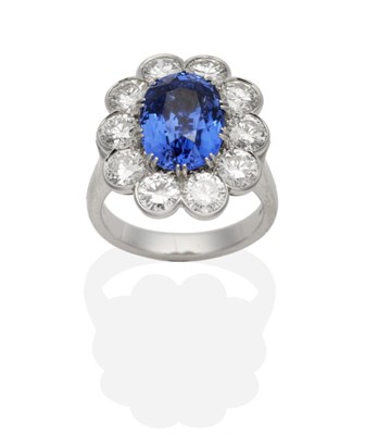 Lot 473 - A Platinum Sapphire and Diamond Cluster Ring, an oval cut sapphire in a double claw setting...