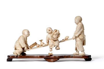 Lot 214 - A Japanese Ivory Figure Group, Meiji period, of a boy sitting on a plank with various objects being