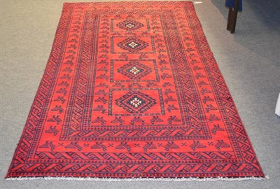 Lot 1232 - Afghan Balouch rug, the rose red field with four panels of hooked devices surrounded by fantail...