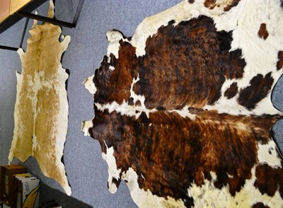 Lot 1091 - A dark brown and white hide rug and a similar rug in light brown