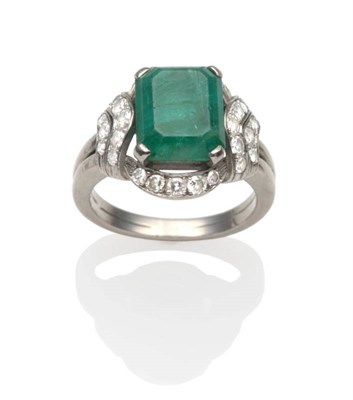 Lot 275 - An Emerald and Diamond Ring, an emerald-cut emerald in a white claw setting within a border of...