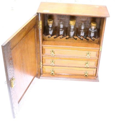 Lot 157 - An Oak Cabinet, containing five glass bottles above three brass handled drawers, behind a...