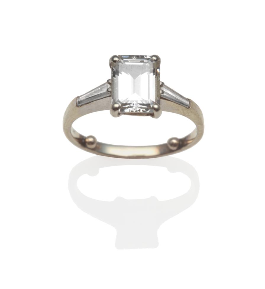 Lot 185 - ~ A Diamond Solitaire Ring, an emerald-cut diamond in a four claw setting, with a tapered...