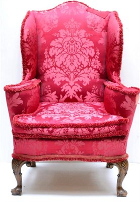 Lot 1180 - A George II Style Walnut Framed Wingback Chair, late 19th century, upholstered in crimson silk...