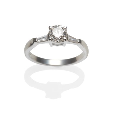Lot 299 - A Platinum Diamond Ring, a round brilliant cut diamond flanked by a tapered baguette cut diamond on