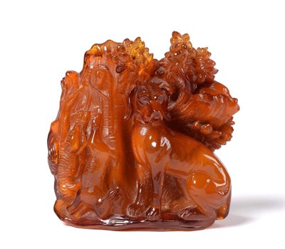 Lot 947 - A German Carved Amber Figure of a Gundog, 19th century, seated before a tree trunk hung with a hare