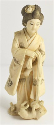 Lot 144 - A Japanese Ivory Okimono, Meiji period, of a young girl in traditional robes playing with a dog...
