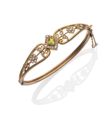 Lot 309 - A Peridot and Seed Pearl Bangle, a square step cut peridot within a border of seed pearls to scroll