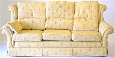 Lot 3180 - A Three-Seater Sofa, upholstered in gold patterned fabric with rounded arm supports and three squab