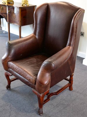 Lot 3210 - A Reproduction Wing Back Armchair, upholstered in close-nailed vintage brown leather, with...