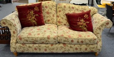 Lot 1170 - A Three-Seater Sofa of recent date, covered in beige and red floral fabric with rounded arms...