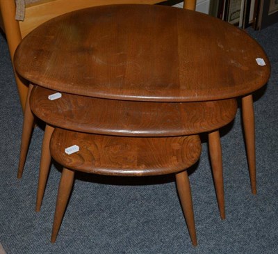 Lot 1149 - A Set of Three Ercol Light Elm Oval Nesting Tables, each raised on three spindle legs, the...