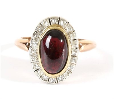 Lot 719 - A Garnet and Diamond Cluster Ring, an oval cabochon garnet in a rubbed over setting, within a...