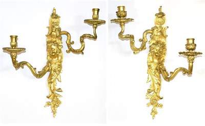 Lot 1016 - A Pair of Gilt Bronze Two-Light Wall Lights, the scroll backplates with cherubs' masks flanked...