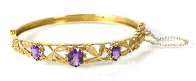 Lot 167 - A 9 carat gold amethyst bangle, three graduated oval cut amethyst in claw settings, between...