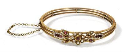 Lot 190 - An early twentieth century ruby and pearl bangle, the front with a floral motif set with round...