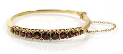 Lot 242 - A 9 carat gold garnet bangle, graduated round cut garnets with single-cut diamond accents, 22.5g