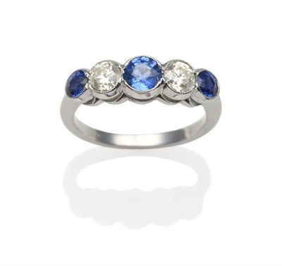 Lot 220 - A Sapphire and Diamond Five Stone Ring, three graduated round cut sapphires spaced by round...