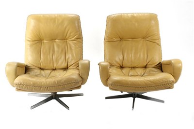 Lot 436 - A Pair of 1970s Mustard Leather Swivel Armchairs, with padded backs and seat between rounded...