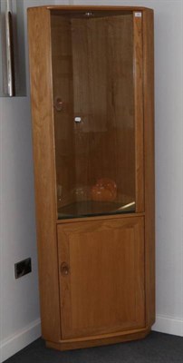 Lot 461 - An Ercol Ash Windsor Corner Cabinet, model 2138, modern, with glazed door enclosing shelves, a...