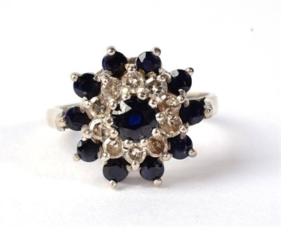 Lot 286 - An 18 carat white gold sapphire and diamond cluster ring, a round cut sapphire within a border...