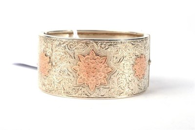 Lot 320 - A Victorian cuff bangle, with three applied rose coloured floral motifs, to a foliate chased front