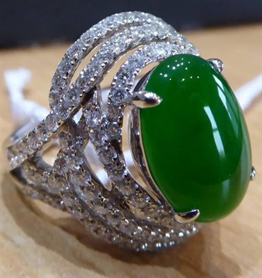 Lot 151 - A Jade and Diamond Cluster Ring, an oval jade in a claw setting, within a pierced scroll border...