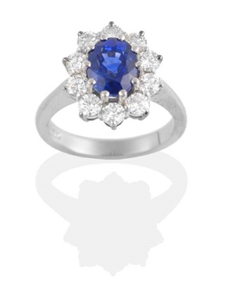 Lot 180 - A Sapphire and Diamond Cluster Ring, an oval cut sapphire in a claw setting, within a border of...