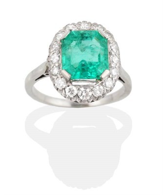 Lot 226 - An Emerald and Diamond Cluster Ring, an octagonal cut emerald in a claw setting within a border...