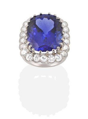 Lot 238 - A Tanzanite and Diamond Cluster Ring, an oval cut tanzanite in a claw setting within a border...