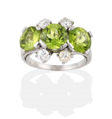 Lot 245 - A Peridot and Diamond Ring, three round cut peridot in claw settings, spaced by pairs of round...