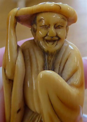 Lot 381 - A Japanese Ivory Netsuke, Edo period, standing holding a lotus leaf on his head, wearing getas...