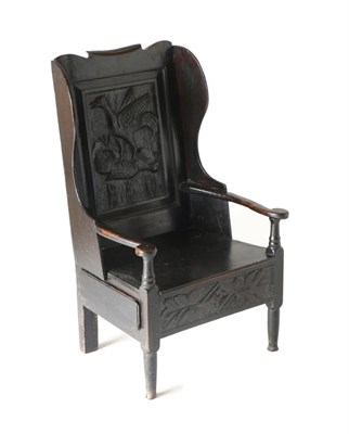 Lot 828 - An 18th Century Joined Oak Wing-Back Chair, the back support carved in relief with two birds...