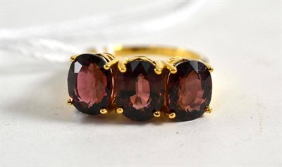 Lot 179 - An 18ct gold rubellite three stone ring, the oval mixed cut stones in yellow claw settings,...