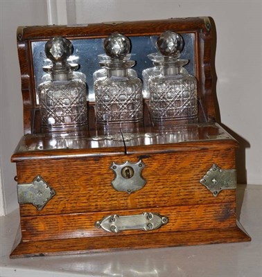 Lot 137 - An Edwardian three bottle tantalus, the oak frame with silver plated mounts, hinged compartment and