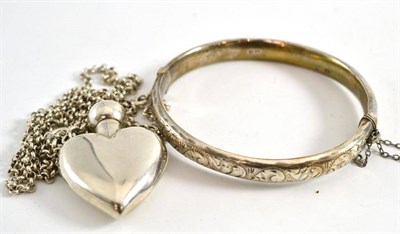 Lot 15 - A silver bangle with engraved decoration and a silver heart perfume/scent bottle pendant on...