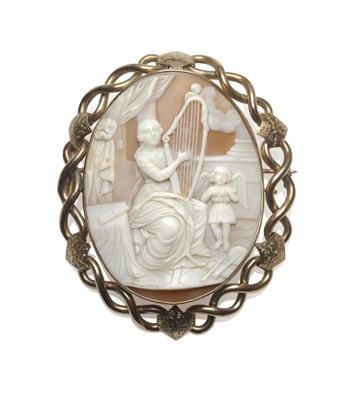 Lot 454 - A Cameo Brooch, the oval shell carved with a scene of a maiden playing the harp, a winged putto...