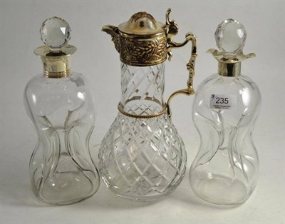 Lot 235 - Two glass decanters with silver mounts, cut glass stoppers and a claret jug with plated mounts (3)