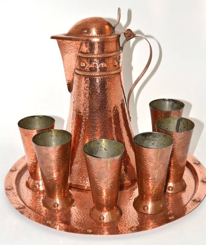 Lot 22 - An Arts & Crafts hammered copper lemonade set, comprising lidded jug, six beakers and a tray