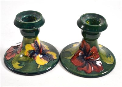 Lot 111 - A pair of Walter Moorcroft hibiscus pattern squat candlesticks, on a green ground, 9cm