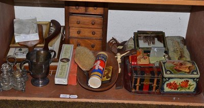 Lot 102 - A shelf of ornamental items including a miniature set of drawers, biscuit tins, plated loving...