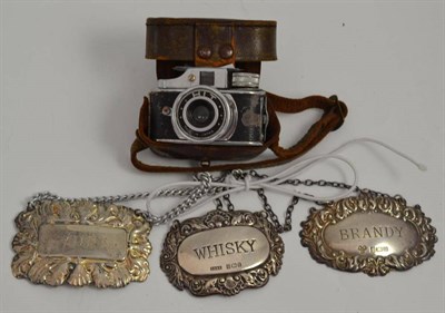 Lot 43 - Two silver bottle tickets, one plated bottle ticket, miniature camera