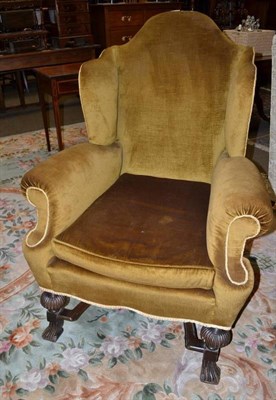 Lot 752 - An early 20th century wingback armchair with oak frame, cross stretchers and gold fabric