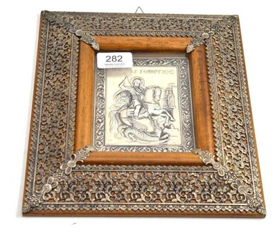 Lot 282 - A white metal plaque depicting St George and The Dragon mounted in a foliate frame 13cm by 10cm