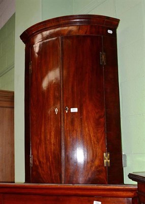 Lot 551 - A George III mahogany bow front hanging corner cupboard with H brass hinges, enclosing shelves